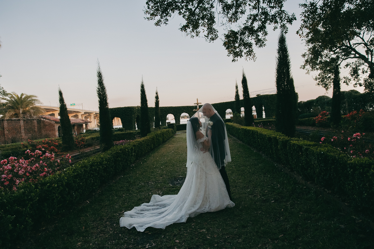 bride and groom kissing underneath veil during twlight with gardens in the background